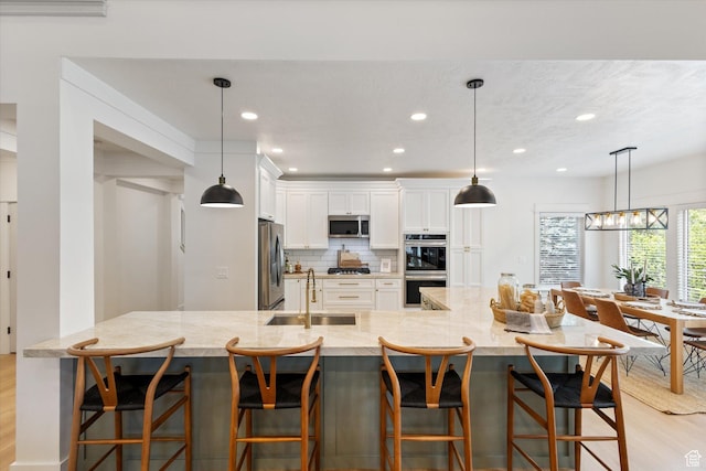 kitchen featuring appliances with stainless steel finishes, a sink, light wood-type flooring, white cabinetry, and tasteful backsplash