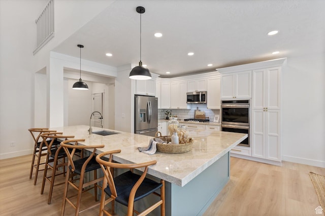 kitchen featuring appliances with stainless steel finishes, a sink, light wood-style flooring, white cabinetry, and decorative backsplash