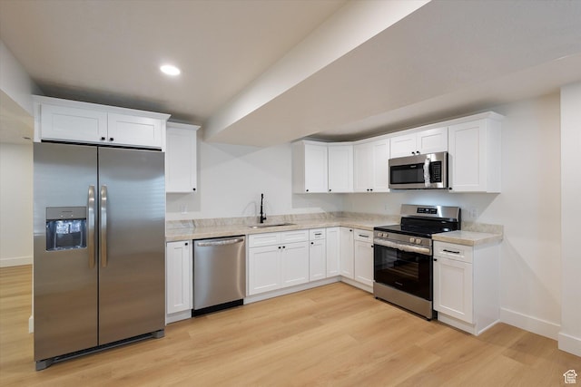 kitchen with appliances with stainless steel finishes, a sink, light wood-type flooring, light countertops, and baseboards