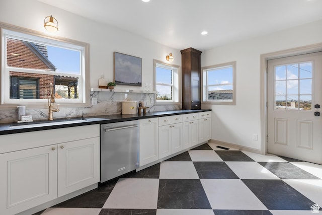 kitchen featuring stainless steel dishwasher, dark countertops, a sink, recessed lighting, and white cabinets