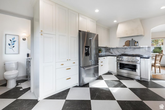 kitchen featuring premium appliances, extractor fan, white cabinets, recessed lighting, and decorative backsplash