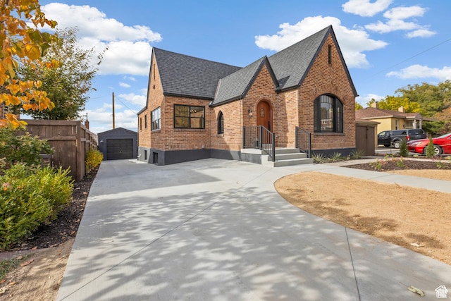 english style home with brick siding, driveway, roof with shingles, an outdoor structure, and a detached garage