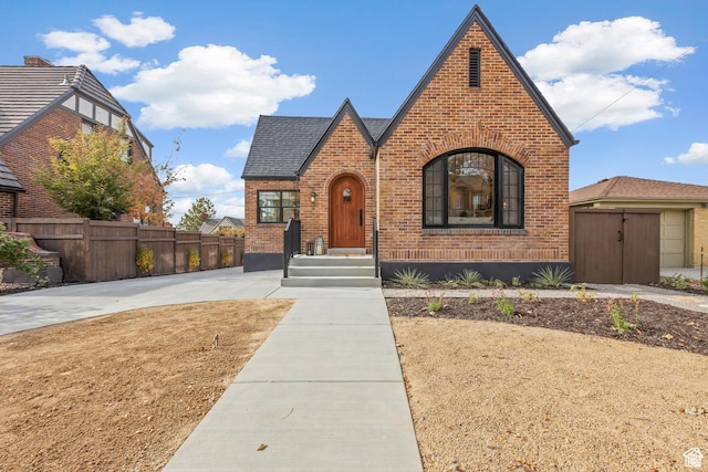 english style home with brick siding, fence, and roof with shingles