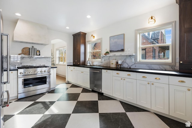 kitchen featuring appliances with stainless steel finishes, range hood, arched walkways, a sink, and decorative backsplash