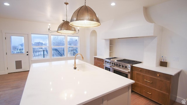 kitchen with double oven range, a sink, light countertops, light wood-type flooring, and recessed lighting