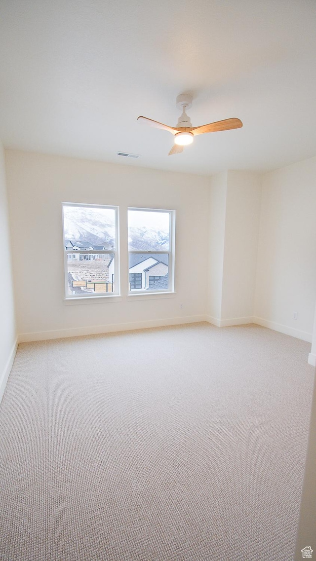 spare room with light colored carpet, baseboards, and a ceiling fan