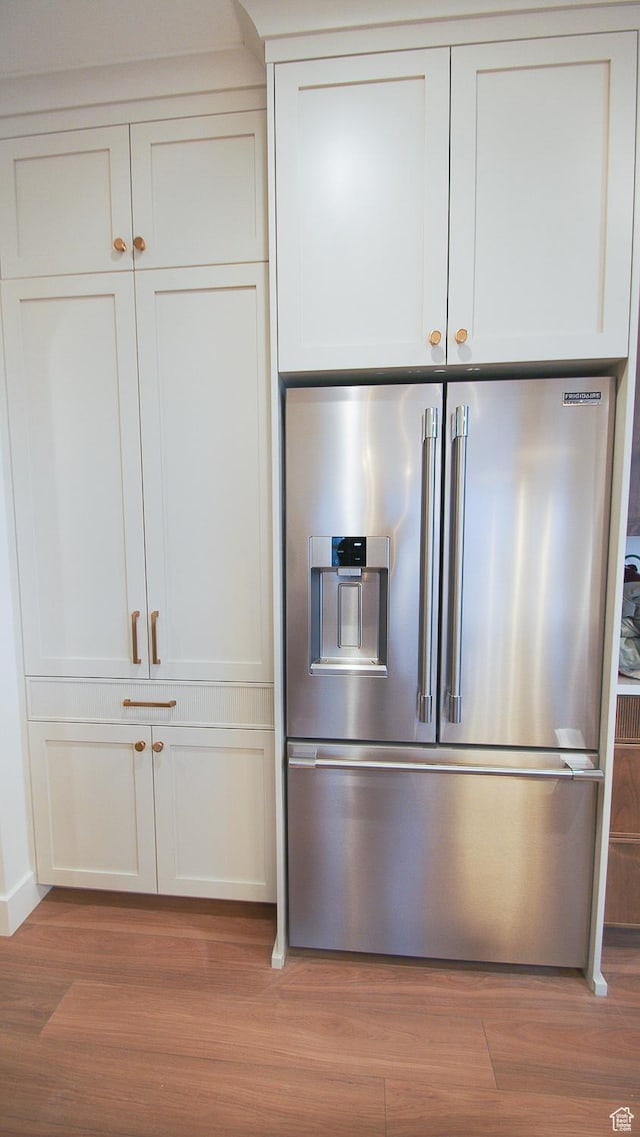 detailed view of high end refrigerator, wood finished floors, and white cabinets