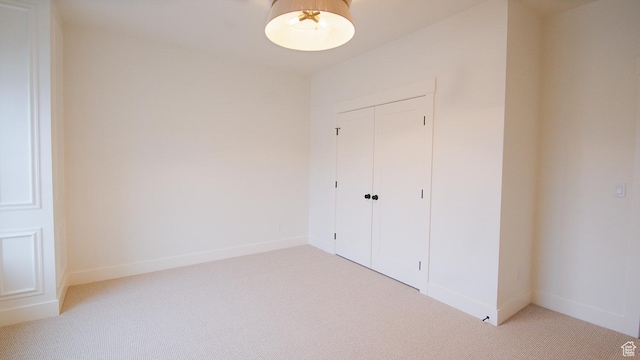 unfurnished bedroom featuring light colored carpet, a closet, and baseboards
