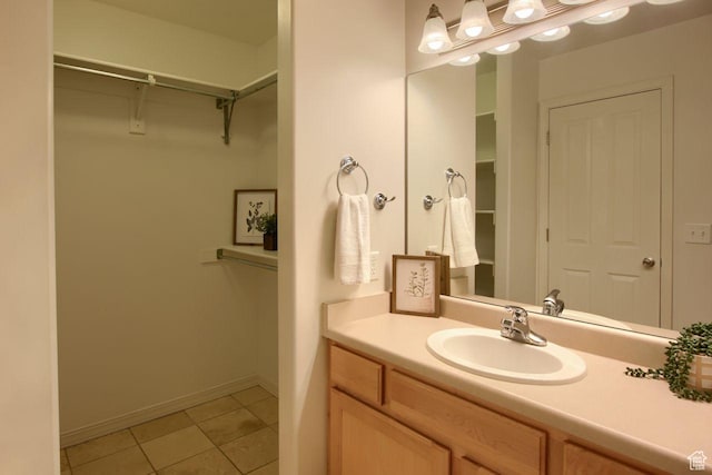 bathroom with tile patterned flooring, a walk in closet, vanity, and baseboards