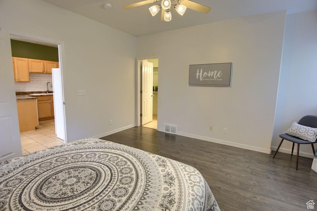 bedroom featuring light wood finished floors, baseboards, ensuite bath, a sink, and ceiling fan