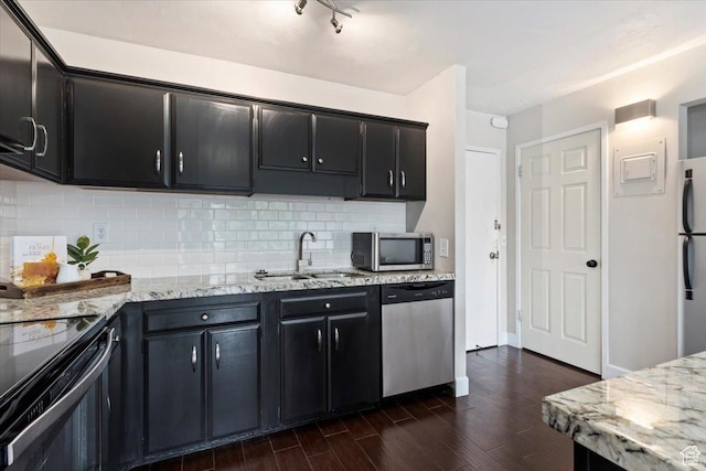 kitchen with appliances with stainless steel finishes, a sink, dark cabinets, dark wood finished floors, and tasteful backsplash