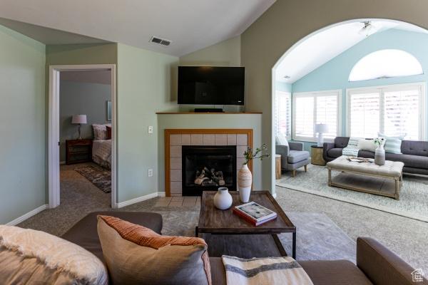living room with lofted ceiling, carpet, a tiled fireplace, and baseboards
