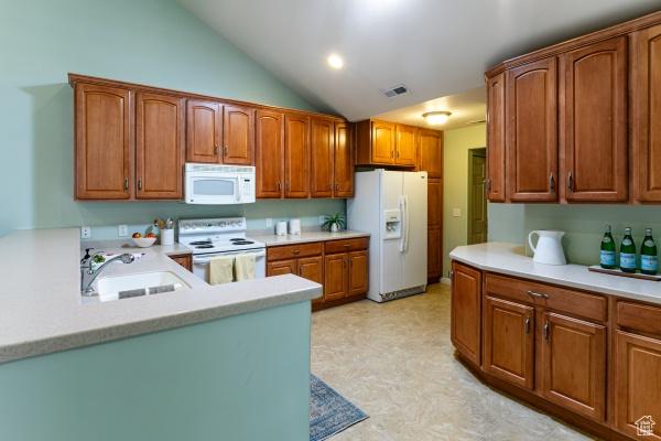 kitchen with white appliances, a sink, light flooring, light countertops, and vaulted ceiling