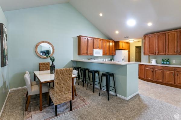kitchen with white appliances, a breakfast bar, light colored carpet, light countertops, and high vaulted ceiling