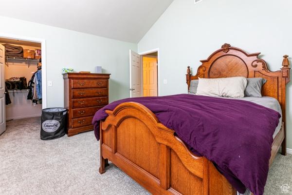 bedroom featuring light colored carpet, lofted ceiling, a closet, and a spacious closet