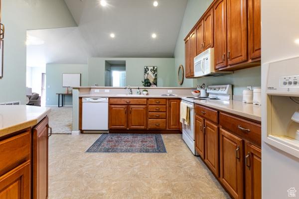 kitchen with white appliances, light countertops, lofted ceiling, and brown cabinets