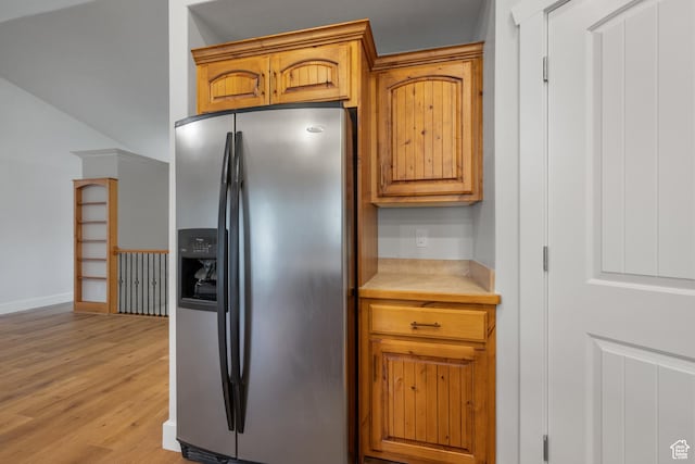 kitchen with stainless steel refrigerator with ice dispenser, light countertops, light wood-style floors, and brown cabinetry
