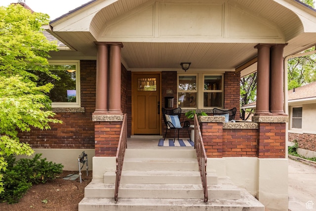 view of exterior entry featuring a porch and brick siding