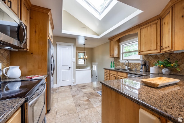 kitchen featuring appliances with stainless steel finishes, a sink, brown cabinets, a skylight, and dark stone counters