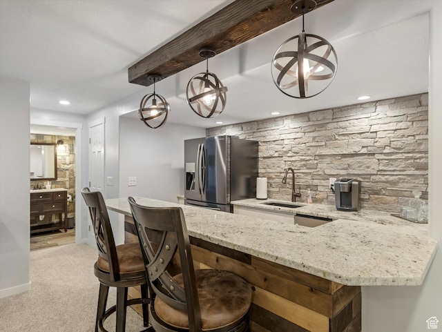 kitchen with stainless steel fridge with ice dispenser, a sink, a kitchen breakfast bar, light stone countertops, and decorative light fixtures