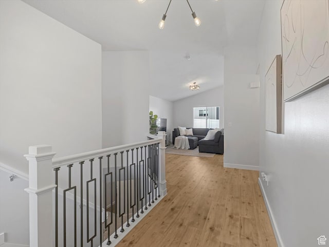 hallway featuring an upstairs landing, wood finished floors, baseboards, and lofted ceiling