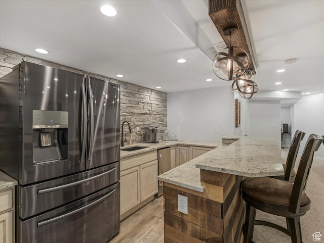 kitchen featuring appliances with stainless steel finishes, a sink, light stone counters, a kitchen bar, and recessed lighting