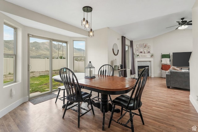 dining space with baseboards, a fireplace, light wood finished floors, vaulted ceiling, and a ceiling fan