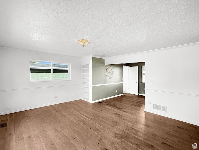 empty room featuring a textured ceiling, wood finished floors, baseboards, and crown molding