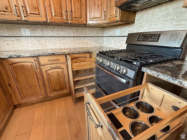kitchen with gas range, tasteful backsplash, brown cabinets, and stone countertops
