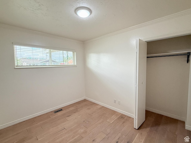 unfurnished bedroom with light wood finished floors, a closet, crown molding, and baseboards