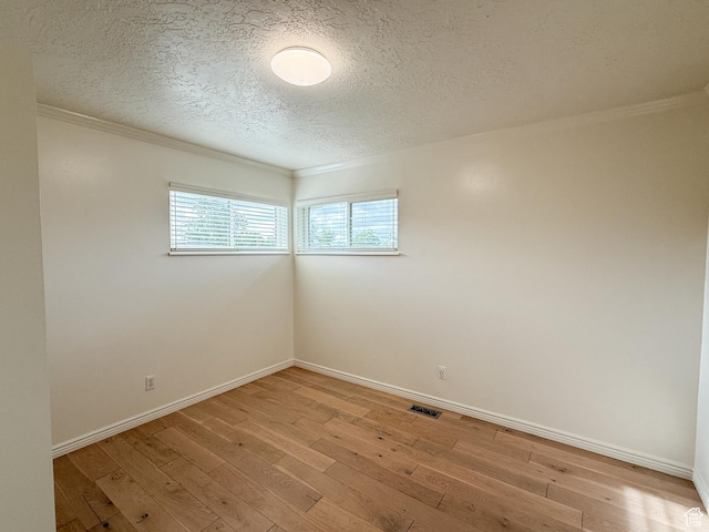 unfurnished room with a textured ceiling, light wood finished floors, ornamental molding, and baseboards