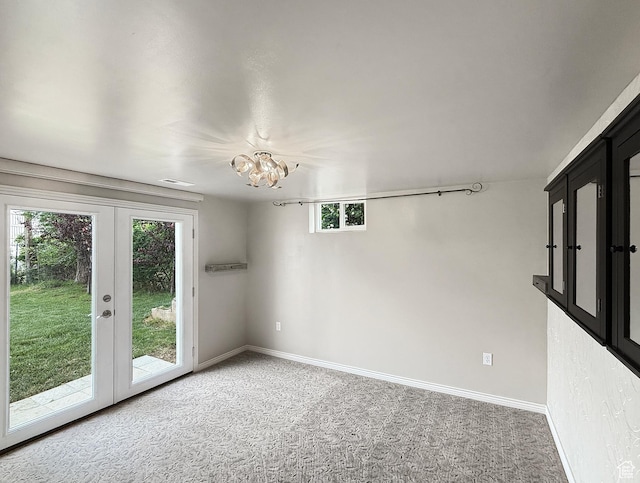 spare room with light colored carpet, french doors, baseboards, and a chandelier