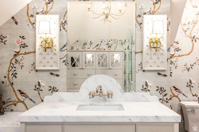bathroom with a chandelier, toilet, vanity, and wallpapered walls