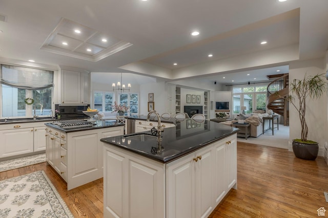 kitchen with an island with sink, dark countertops, a raised ceiling, light wood-type flooring, and recessed lighting