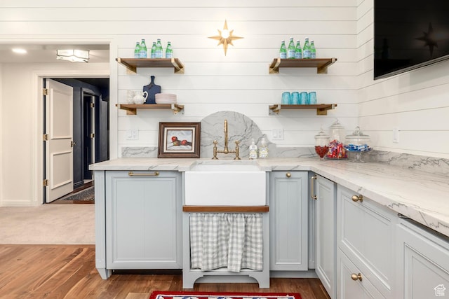 kitchen featuring open shelves, wood finished floors, light stone counters, and wooden walls