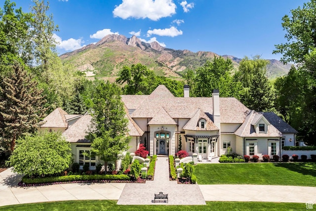french provincial home featuring a chimney, a front lawn, stucco siding, a mountain view, and french doors