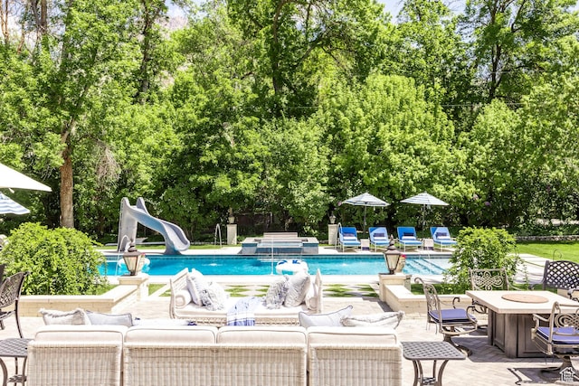 outdoor pool with a water slide, outdoor lounge area, a patio, and view of scattered trees