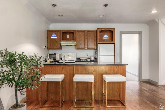 kitchen with freestanding refrigerator, under cabinet range hood, dark countertops, brown cabinetry, and recessed lighting