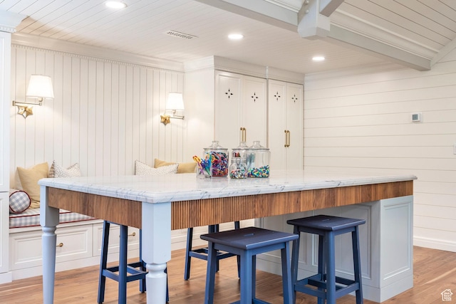 kitchen with a breakfast bar, light wood-style floors, wood walls, recessed lighting, and white cabinets