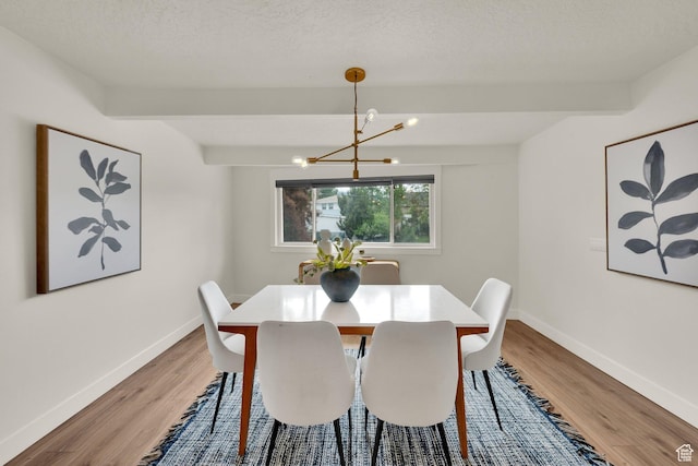 dining area with a chandelier, light wood finished floors, baseboards, beam ceiling, and a textured ceiling