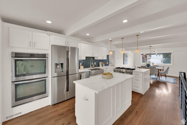 kitchen with stainless steel appliances, a peninsula, beam ceiling, a center island, and white cabinetry