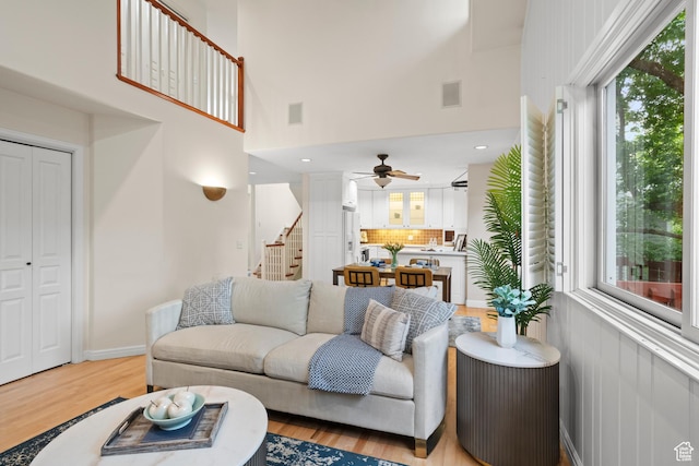 living area featuring stairway, ceiling fan, light wood finished floors, and a towering ceiling
