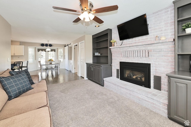 carpeted living room featuring a ceiling fan, a brick fireplace, and built in shelves