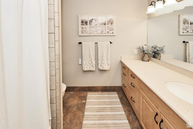bathroom featuring stone tile flooring, vanity, baseboards, and toilet