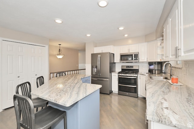 kitchen with appliances with stainless steel finishes, a sink, a breakfast bar area, white cabinetry, and a kitchen island