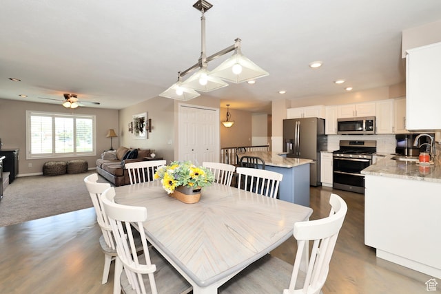 carpeted dining area with a sink, a ceiling fan, baseboards, and wood finished floors