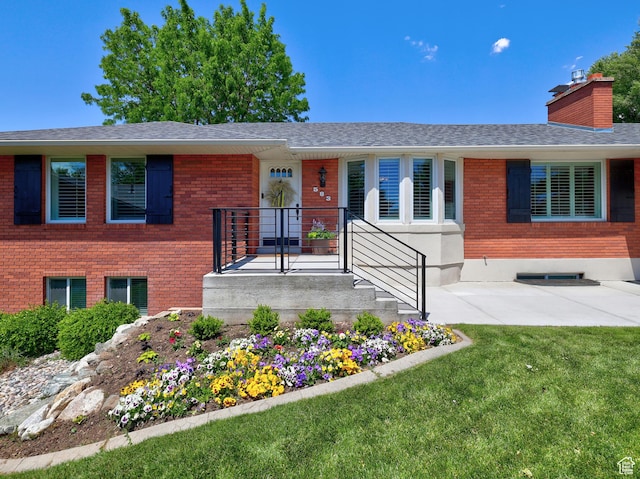view of front of house featuring brick siding, a front yard, roof with shingles, and a chimney