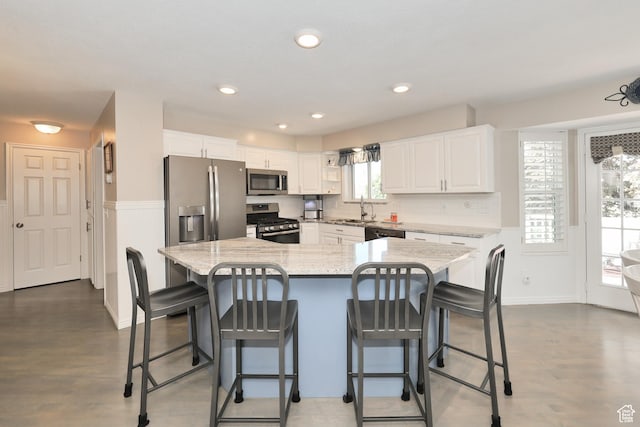 kitchen with stainless steel appliances, white cabinets, a sink, light stone countertops, and a breakfast bar area