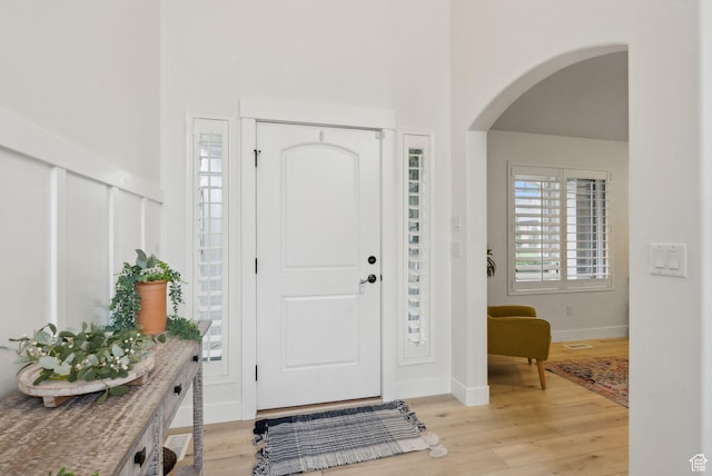 entryway featuring arched walkways, light wood-type flooring, a high ceiling, and baseboards