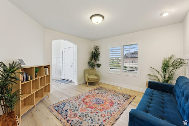 living room with arched walkways, light wood-style floors, and baseboards